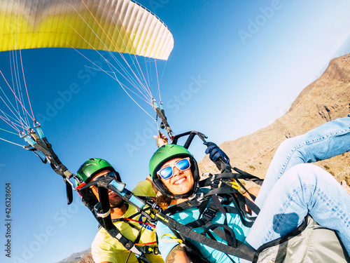Active young adult people woman enjoy paraglide activity fliying in the sky with professional pilote in the back - cheerful happy female people fly and have fun with paragliding photo