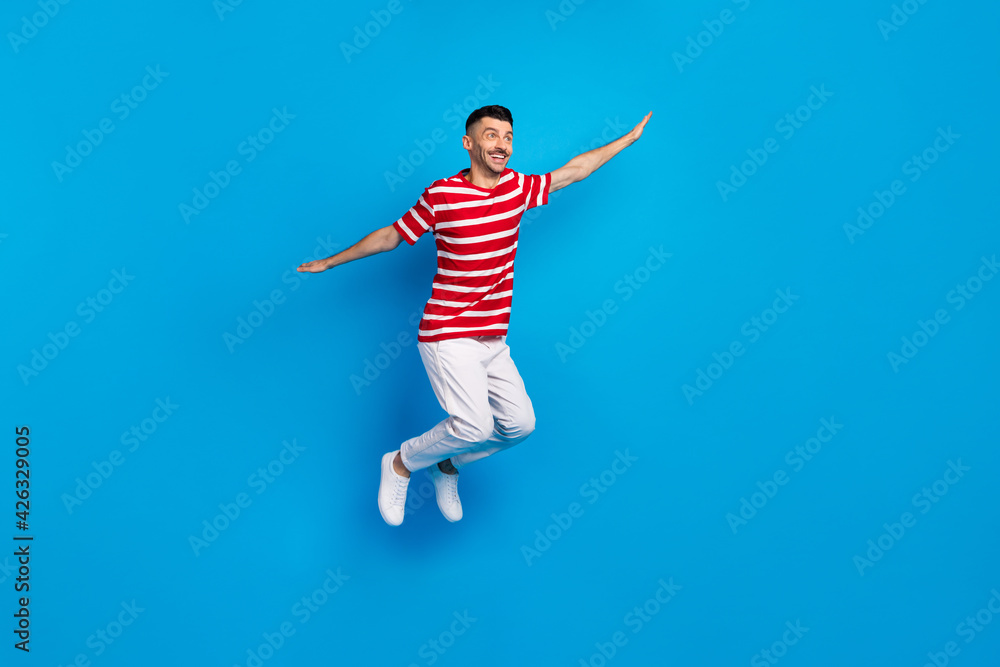 Photo of dreamy sweet young man wear striped t-shirt jumping looking empty space isolated blue color background Photo of dreamy sweet young man wear striped t-shirt jumping looking empty space isolated blue color background