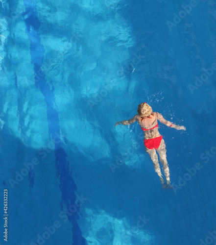 A girl in a red swimsuit swims in a pool with blue water.