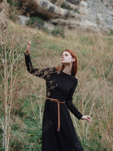 Red-haired Woman in a black dress are walking on nature in autumn in the forest