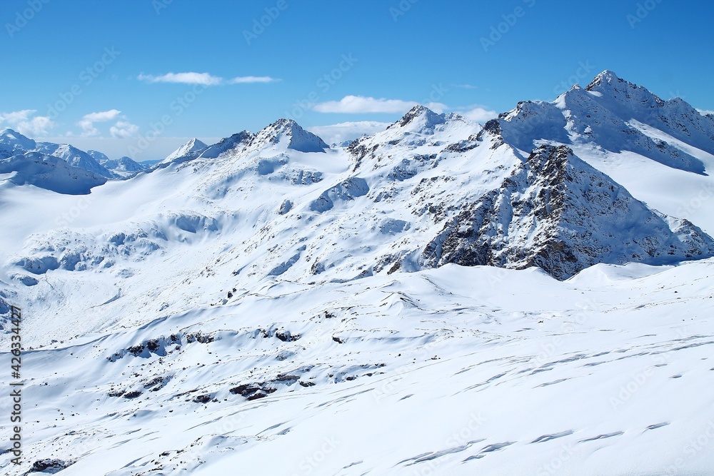 Peaks of snow-capped mountains. Snow in the mountains. Sun in the mountains. The slopes of the snow-capped mountains. Picturesque mountain views. Travel to the mountains. Mountains in the snow. 