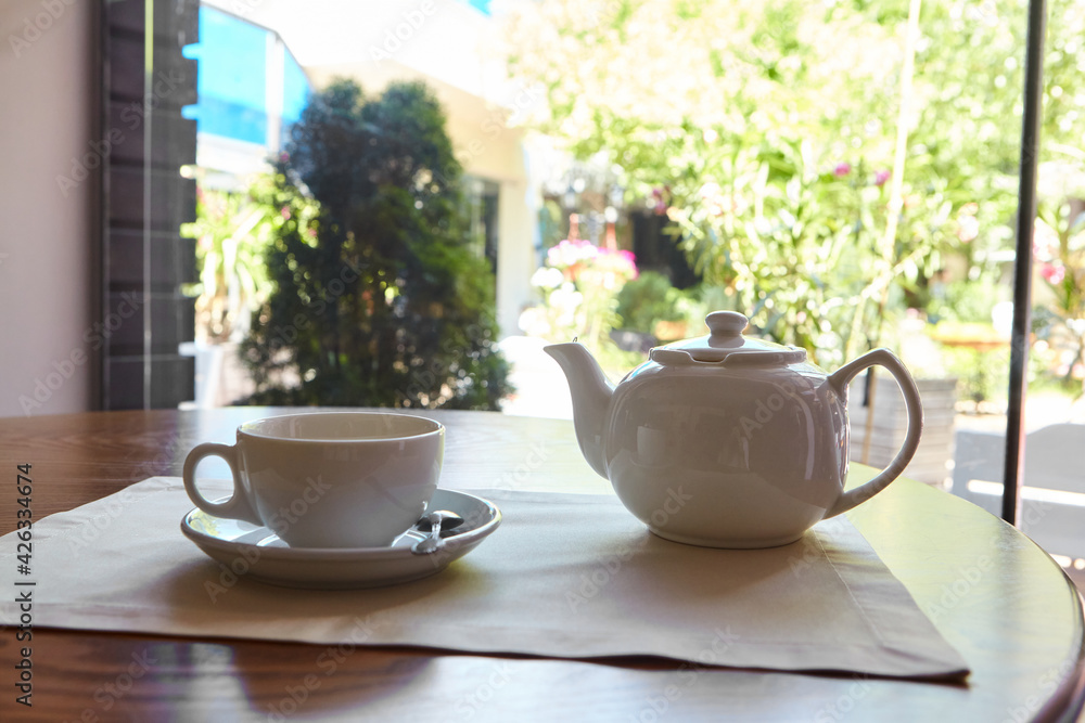 The table is set for tea. A teapot and a tea cup are placed on the table overlooking the terrace The table is set for tea. A teapot and a tea cup are placed on the table overlooking the terrace