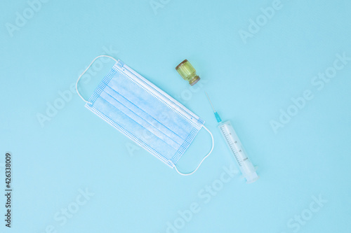 Medical mask, syringe and jar on a blue background. A disposable surgical face mask covers the mouth and nose. Healthcare and medical concept.