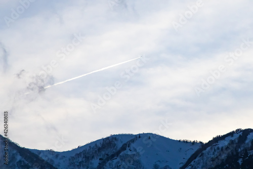 春の日光の雪山の上の美しい飛行機雲