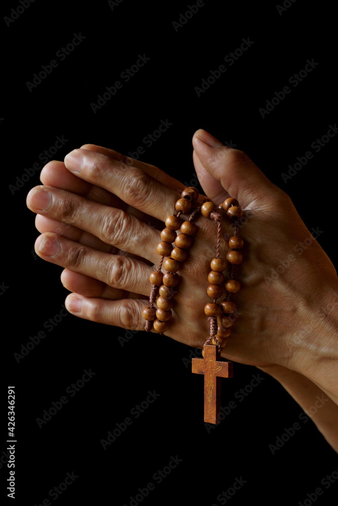 Praying hands of Indian Catholic woman with wooden rosary isolated on a black background. Praying hands of Indian Catholic woman with wooden rosary isolated on a black background.