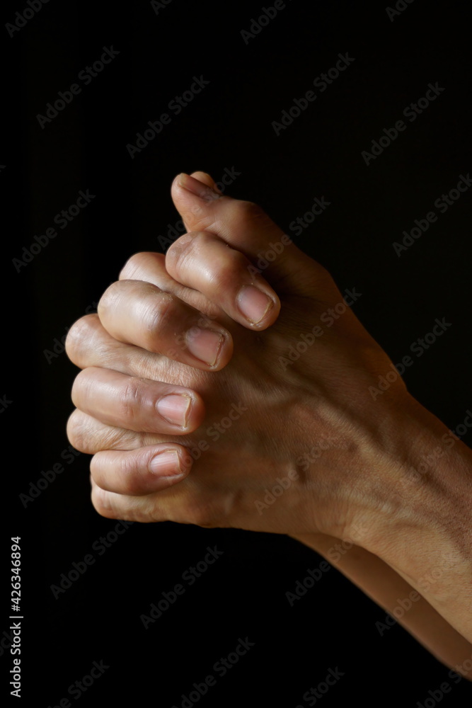 Praying hands of an old Indian Catholic woman isolated on a plain black background.