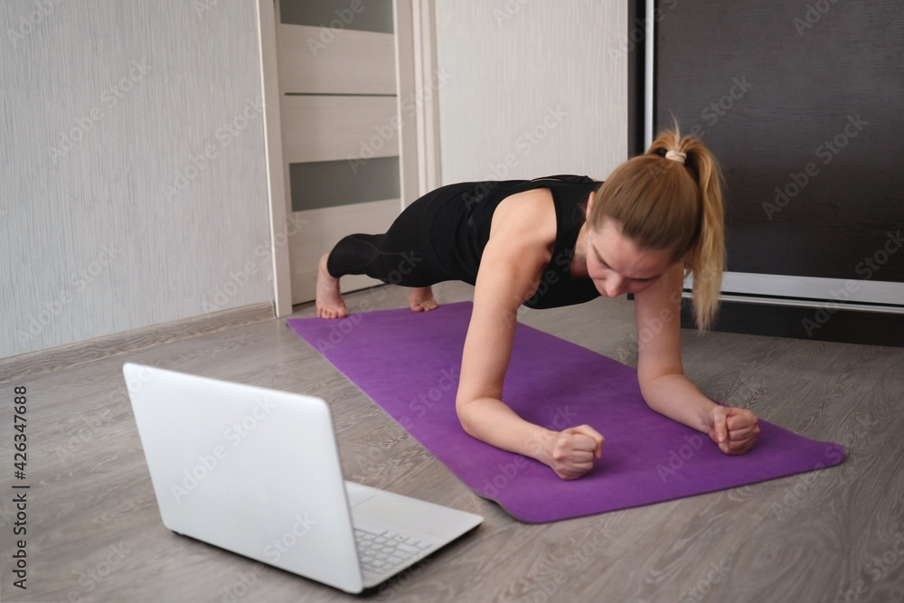 young woman doing asana at home on yoga mat in front of laptop young woman doing asana at home on yoga mat in front of laptop