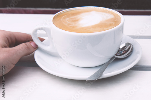 Cappuccino in a white ceramic cup on a white wooden bench. Open-air rustic morning coffee