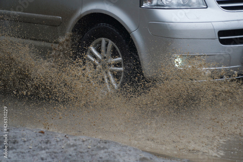  Car quickly go through a puddle throwing out splashes and water from under the wheels.