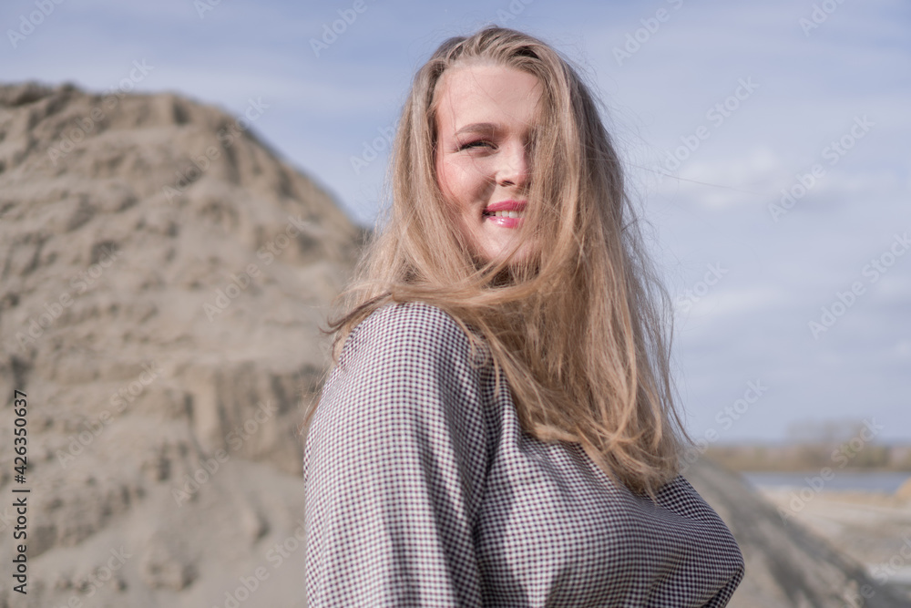 Beauty portrait of a young blond girl in a vintage dress. She is posing on a sandy landscape.
