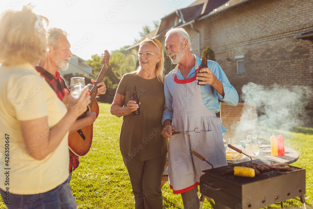 Obraz premium Elderly people playing the guitar and singing while having backyard barbecue party