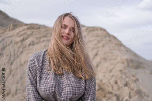 Beauty portrait of a young blond girl in a vintage dress. She is posing on a sandy landscape. © Stock Rocket