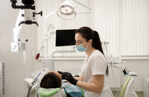 A woman dentist in gloves and a medical mask operates on a patient using equipment - a microscope. The office of a modern dentist.