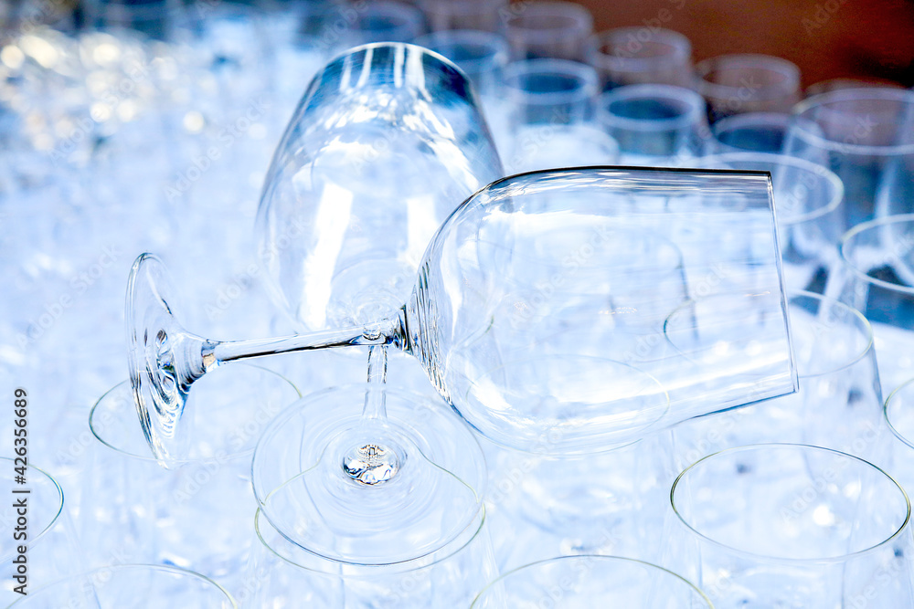 Two red wine crystal glasses lay on a raw of other grasses prepared for big party. Blurred. Catering and restaurant utensils. wedding organisation. Wine tasting. Background picture. Group of objects 