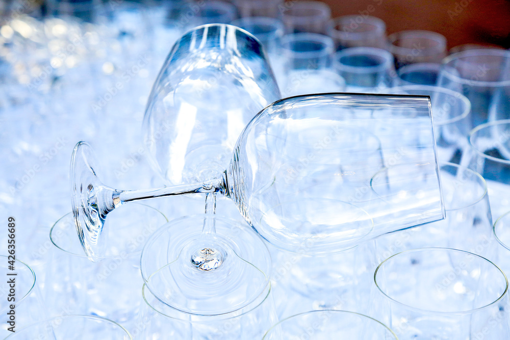Two red wine crystal glasses lay on a raw of other grasses prepared for big party. Blurred. Catering and restaurant utensils. wedding organisation. Wine tasting. Background picture. Group of objects Two red wine crystal glasses lay on a raw of other grasses prepared for big party. Blurred. Catering and restaurant utensils. wedding organisation. Wine tasting. Background picture. Group of objects