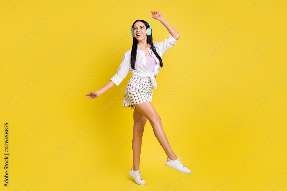 Full size photo of young pretty smiling cheerful positive girl dancing in headphones isolated on yellow color background Full size photo of young pretty smiling cheerful positive girl dancing in headphones isolated on yellow color background