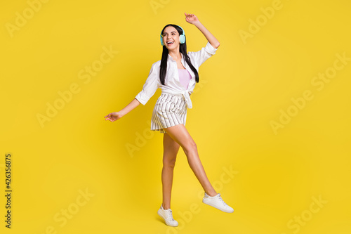 Full size photo of young pretty smiling cheerful positive girl dancing in headphones isolated on yellow color background