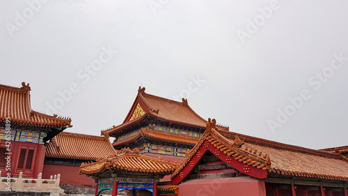 A close up on a building complex inside of Forbidden City in Beijing, China. The buildings have very richly decorated rooftops, with elements of gold. White marble railing in front of them. Royalty