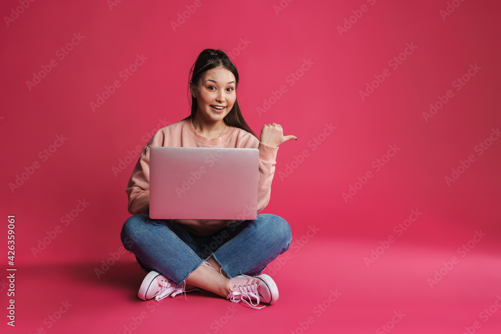 Asian smiling woman pointing finger aside and using laptop Asian smiling woman pointing finger aside and using laptop