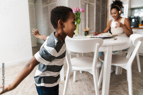 Black boy running and making fun while her mother working at table
