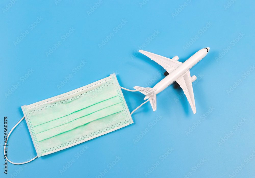 Top view or flat lay of airplane model and medical face mask on blue background. Traveling during covid-19 epidemic concept.