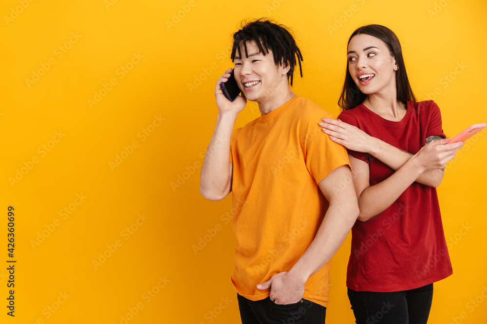Young multiracial couple smiling while using and talking on cellphones Young multiracial couple smiling while using and talking on cellphones