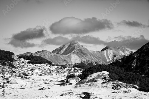 Sunny winter day in High Tatra Mountains, Poland. Peaks on Slovak side covered with big white clouds. Selective focus on the rocks, blurred background.