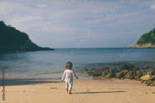 Cute little child at the empty beach go to the sea. Zen, lifestyle and wellbeing concept. Small toddler girl walking on sea shore alone. Barefoot kid at early morning. Photo with copy space