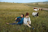 Hipster couple of bearded young man and girl with dreadlocks posing in the fields with cows on the background. Human and nature