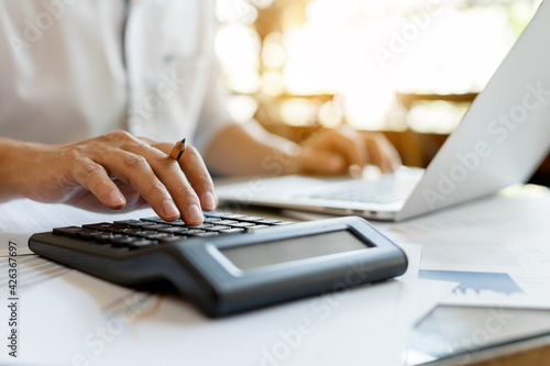 Close up businessman pressing on calculator for calculating cost estimating with laptop. photo