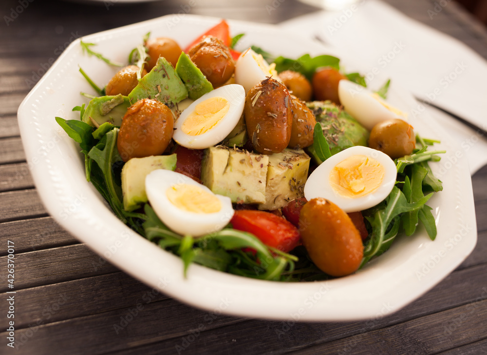 dish of fresh vegetables arugula, avocado, cherry tomatoes with olives and quail eggs on dining table