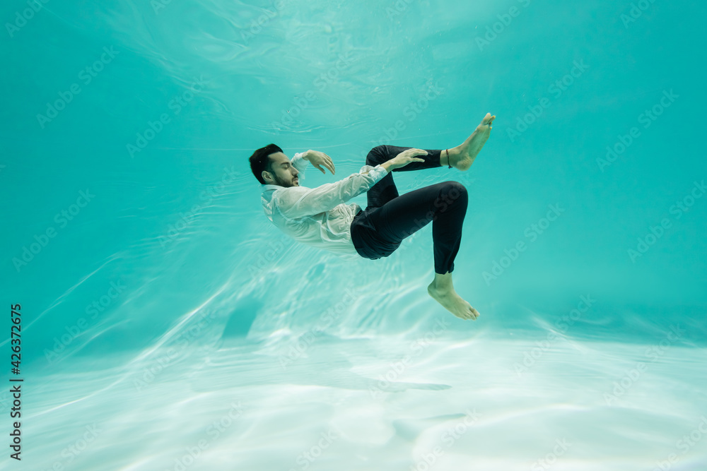Arabian businessman in pants and shirt swimming underwater in pool