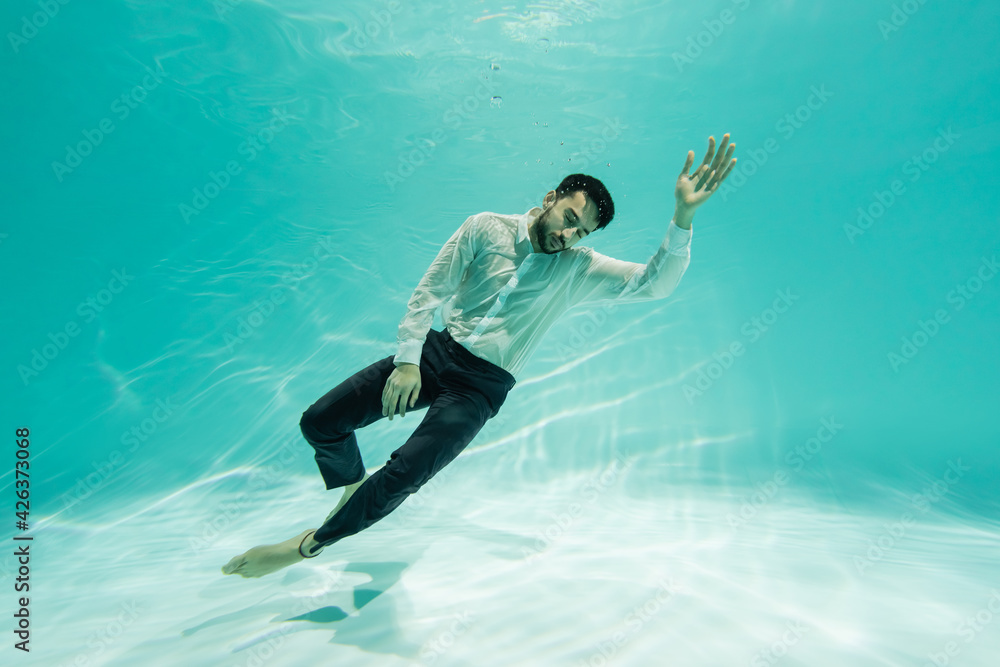 Arabian businessman in formal wear swimming near bottom of pool