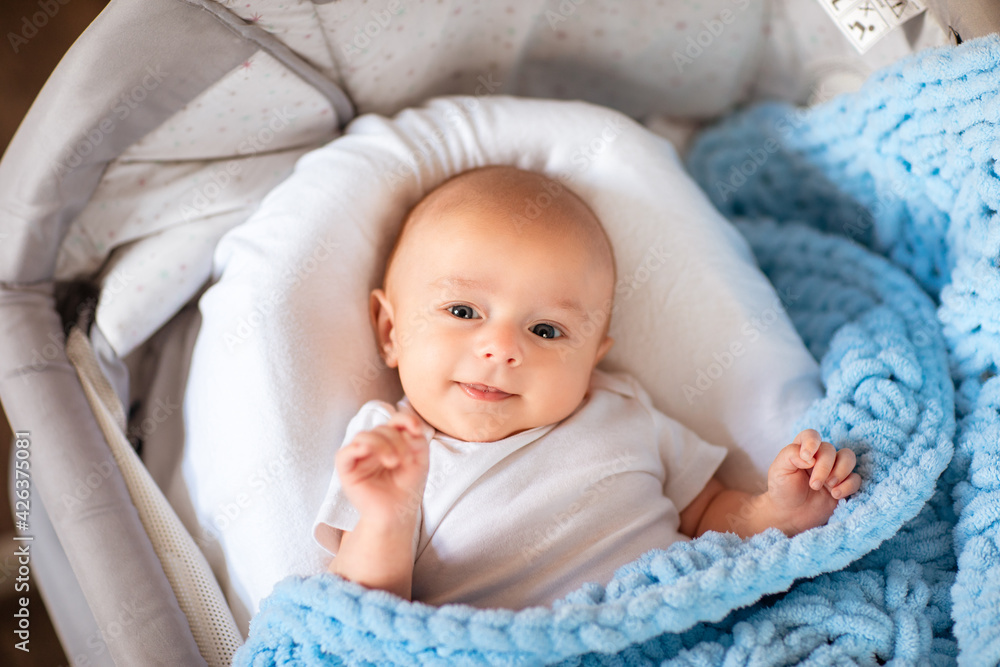 Cute newborn baby boy in white body laying in his cradle with soft blue blanket. Cute newborn baby boy in white body laying in his cradle with soft blue blanket.