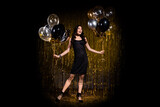 Photo of charming impressed young woman dressed black outfit holding balloons isolated gold shine backdrop background