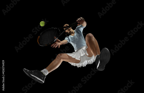 Female professional tennis player in action, motion isolated on black background, look from the bottom. Concept of sport, movement, energy and dynamic. © master1305