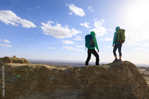 Two successful women backpackers standing on the top frozen soil hill top