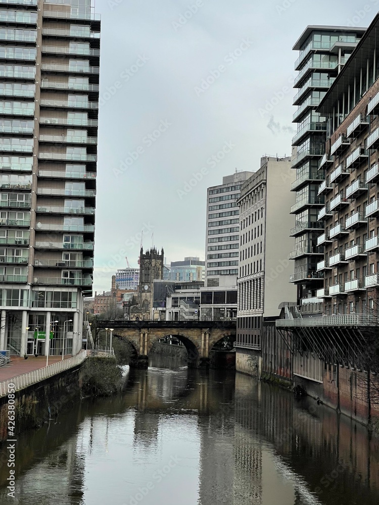 A river running through Manchester City centre with modern architecture and landmark buildings. 