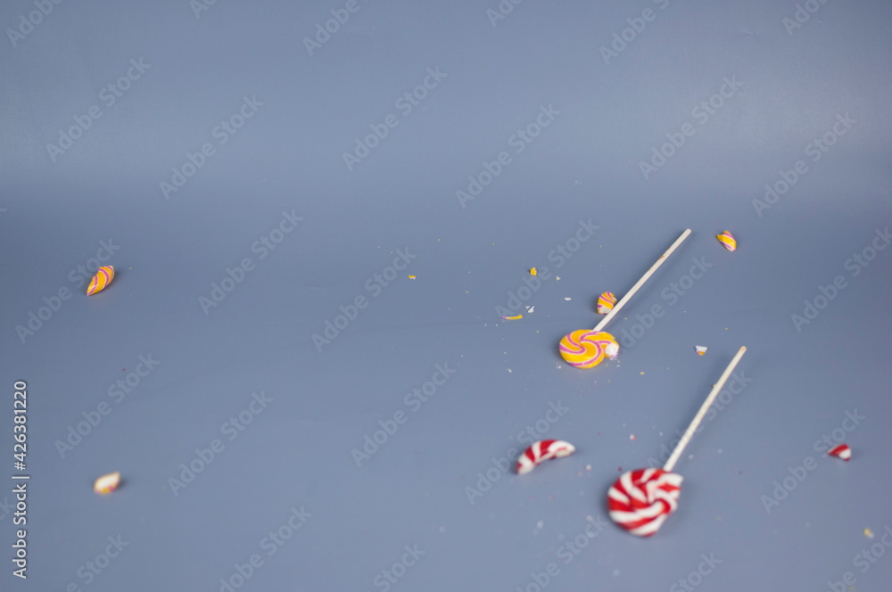 Broken in pieces candy on a stick. Smashed lollipop on grey background, top view with copy space. Broken in pieces candy on a stick. Smashed lollipop on grey background, top view with copy space.