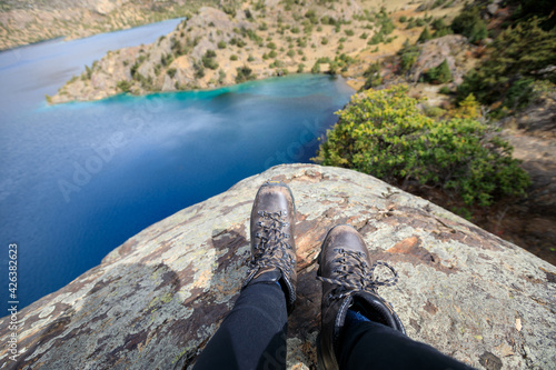 Woman hiker sit on cliff edge facing the beautiful high altitude lake