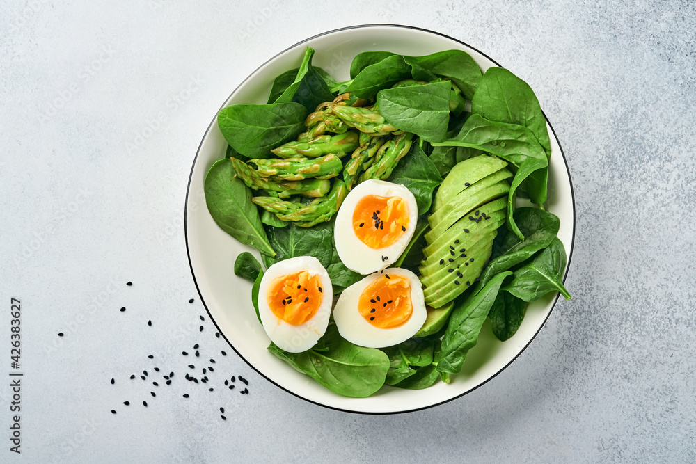 Fresh vegetable salad with avocado, asparagus, crumpled eggs with black sesame seeds and spinach on plate on light slate, stone or concrete background. Balanced lunch in bowl. Top view. Mock up. Fresh vegetable salad with avocado, asparagus, crumpled eggs with black sesame seeds and spinach on plate on light slate, stone or concrete background. Balanced lunch in bowl. Top view. Mock up.