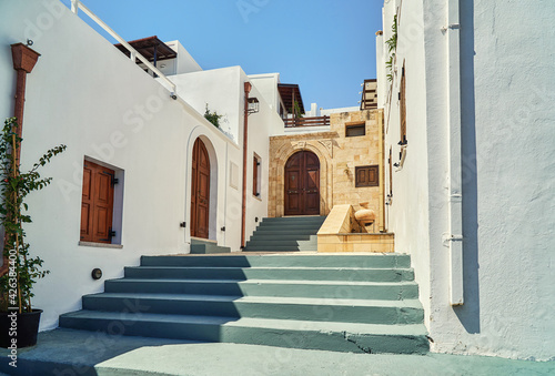Weathered grey stairs and white historical buildings with wooden doors on Lindos town street at sunlight on summer day in Greece