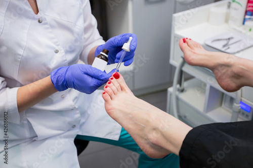 Fotografia Pedicure master applies remedy to young woman's nails in a nail salon