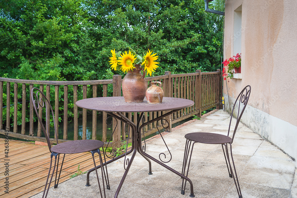 One table and two chairs on terrace. Bunch of sunflowers on the metallic table