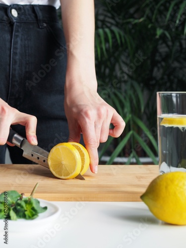 Woman cutting lemon on wooden board. Detox water with mint and lemon. Refreshing summer drink. Wellness, diet, healthy eating concept