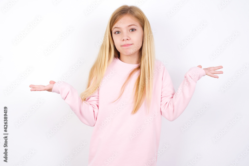 Maybe yes or no. Doubtful beautiful caucasian little girl wearing pink hoodie over white shrugs shoulders in bewilderment, tries to make decision puzzled what he wants. Hesitation and uncertainty. Maybe yes or no. Doubtful beautiful caucasian little girl wearing pink hoodie over white shrugs shoulders in bewilderment, tries to make decision puzzled what he wants. Hesitation and uncertainty.