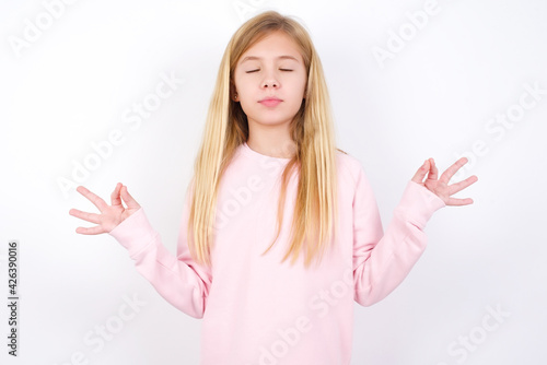 Wallpaper Mural beautiful caucasian little girl wearing pink hoodie over white background doing yoga, keeping eyes closed, holding fingers in mudra gesture. Meditation, religion and spiritual practices. Torontodigital.ca