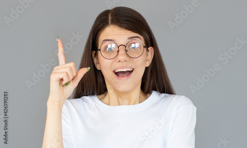 Photo of energetic nice smiling lady wearing white t-shirt isolated on gray background pointing her finger in eureka sign  having great innovative idea  understanding or solution she has just got.