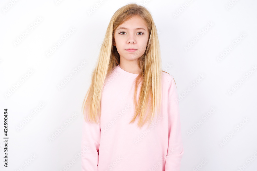 Joyful beautiful caucasian little girl wearing pink hoodie over white background looking to the camera, thinking about something. Both arms down, neutral facial expression. Joyful beautiful caucasian little girl wearing pink hoodie over white background looking to the camera, thinking about something. Both arms down, neutral facial expression.