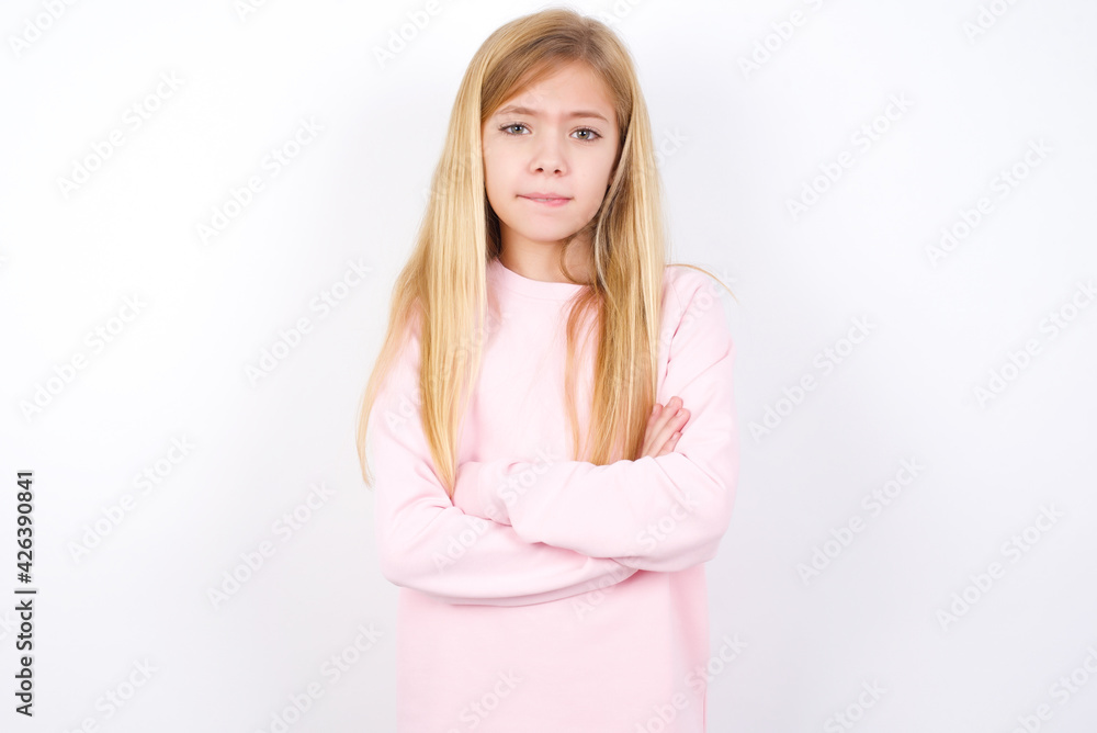 beautiful caucasian little girl wearing pink hoodie over white background bitting his mouth and looking worried and scared crossing arms, worry and doubt. beautiful caucasian little girl wearing pink hoodie over white background bitting his mouth and looking worried and scared crossing arms, worry and doubt.